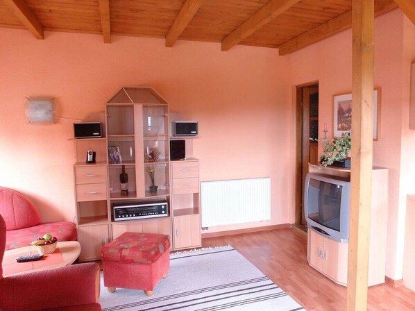 Una sala de estar acogedora con techo de madera, un aparador de vidrio, un televisor y un sofá rojo.