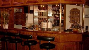 Een bar met houten lambrisering, een toog en drie barkrukken.