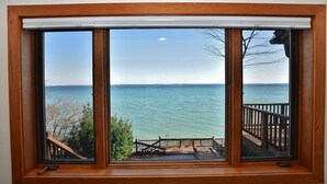 A large window with a view of the sea, a wooden deck, and a railing. - Luxury Bayfront Retreat on Grand Traverse Bay with Private Beach and Sport Court (Suttons Bay)