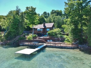 Une propriété au bord du lac, dotée d’un quai, d’une terrasse couverte et d’une grande maison entourée d’arbres.