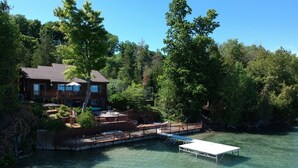 A lakeside property with a dock, a boat, and a house with a deck. - Luxury Bayfront Retreat on Grand Traverse Bay with Private Beach and Sport Court (Suttons Bay)