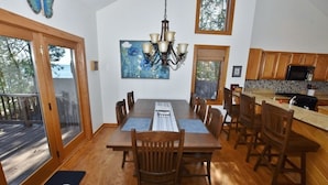 A dining area with a wooden table, chairs, a chandelier, and a view of the outdoors through large windows. - Luxury Bayfront Retreat on Grand Traverse Bay with Private Beach and Sport Court (Suttons Bay)