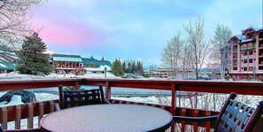 Varanda com mesa e cadeiras, vista para uma paisagem nevada com edifícios ao fundo.