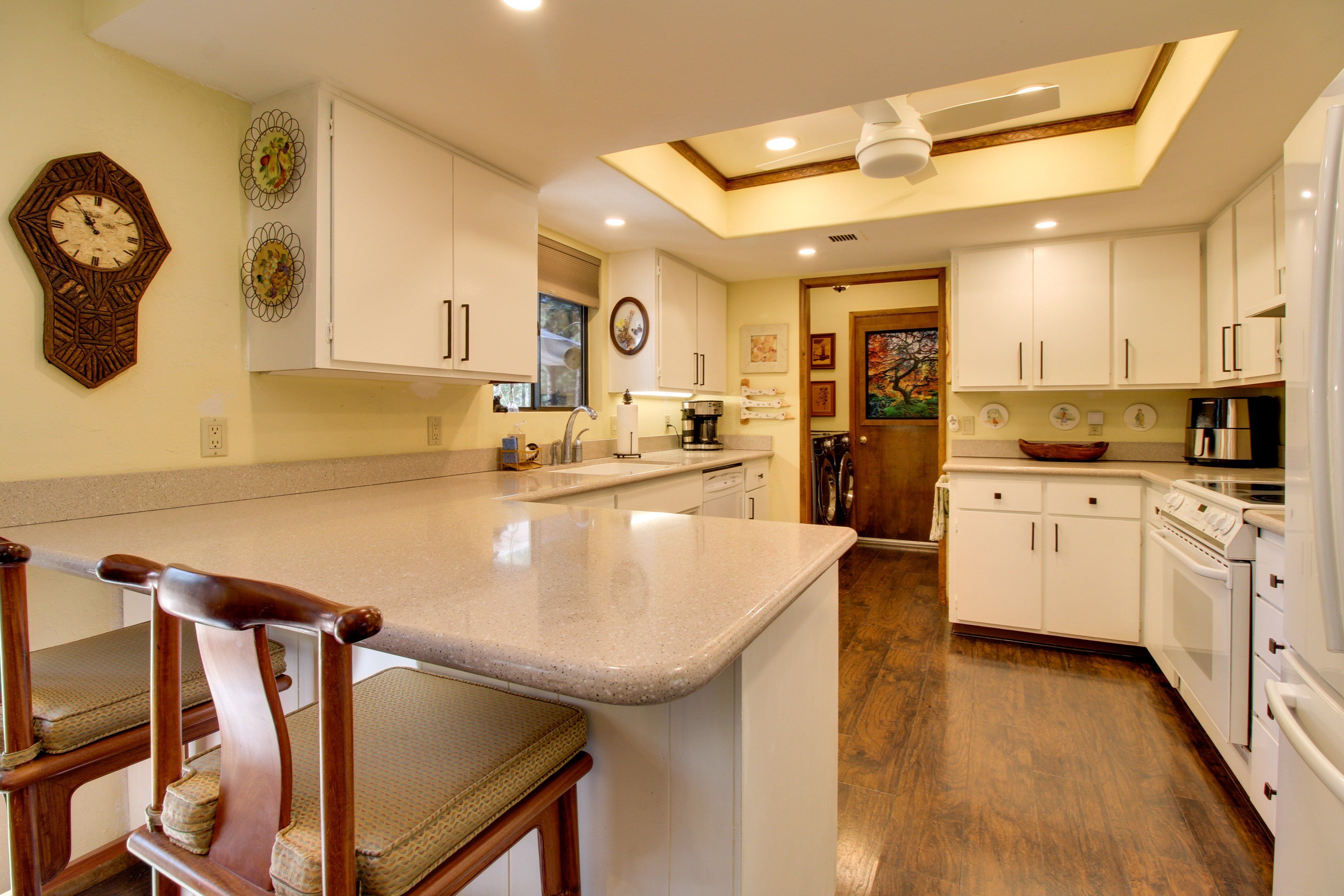 A kitchen with white cabinets, a wooden chair, and a clock on the wall.