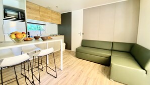 A modern kitchen with white bar stools, a green sofa, and a wooden cabinet. - See Breizh Camping La Ville Huchet (Saint-Malo)