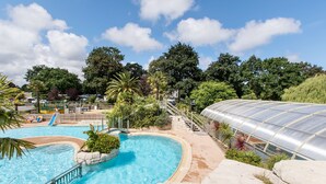 A swimming pool with a slide, surrounded by greenery and a greenhouse structure. - See Breizh Camping La Ville Huchet (Saint-Malo)