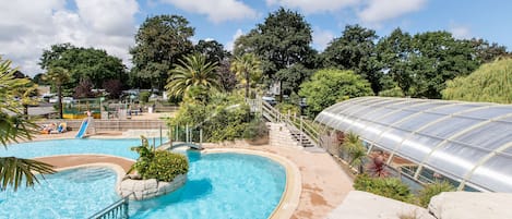 A swimming pool with a slide, surrounded by greenery and a greenhouse structure.
