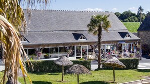 A restaurant with a thatched roof, outdoor seating, and a view of a green field. - See Breizh Camping La Ville Huchet (Saint-Malo)