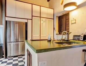 A kitchen with a stainless steel refrigerator, a sink, and a window with blinds.