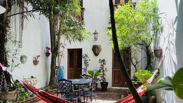 A courtyard with a brick floor, a hammock, a table with chairs, and various potted plants. - Quaint Colonial Home in Old San Juan (San Juan)