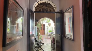 A corridor with a checkered floor, wooden doors, and a view of an outdoor patio area with chairs and tables. - Quaint Colonial Home in Old San Juan (San Juan)