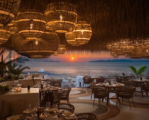 A restaurant with wicker furniture and a view of the sunset over the sea. - Andronis Arcadia Hotel (Santorini)