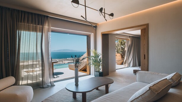 A modern living room with a sofa, a coffee table, and a view of the ocean. - Andronis Arcadia Hotel (Santorini)