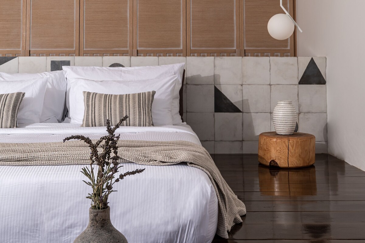 Un dormitorio moderno con una cama grande, cabecera de madera y una lámpara colgante minimalista.