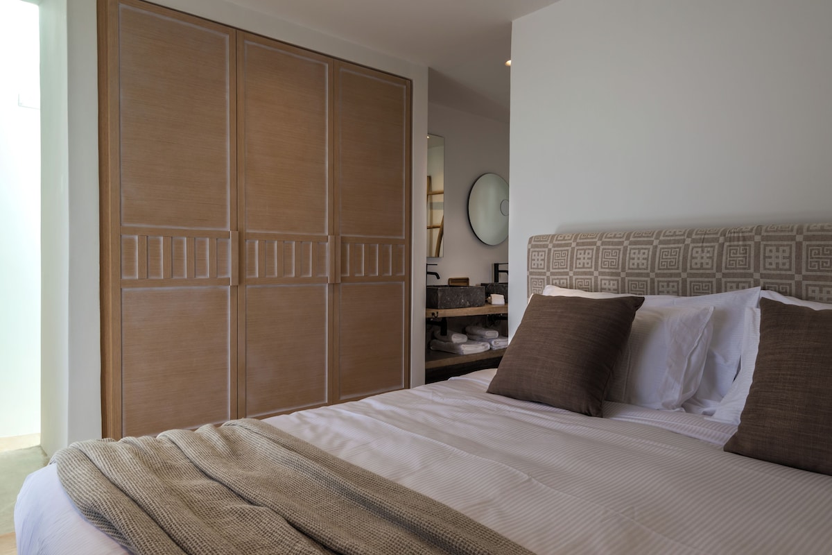 A bedroom with a large bed, a wardrobe, a mirror, and a shelf with towels.