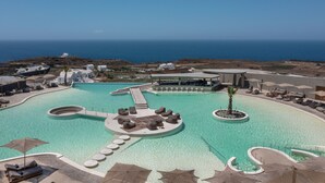 A resort pool with a central island, sun loungers, and a view of the ocean. - Andronis Arcadia Hotel (Santorini)