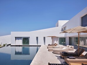 A modern poolside area with lounge chairs and umbrellas, a clear blue sky, and a white building.