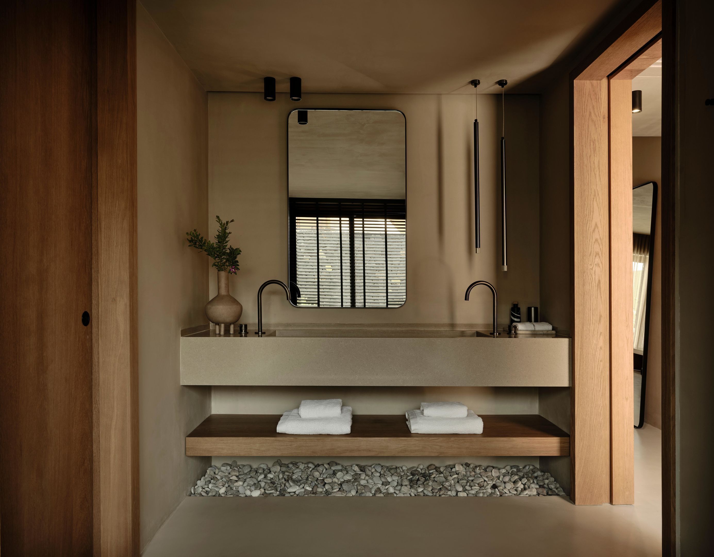 A modern bathroom with a wooden vanity, a large mirror, and a built-in shelf with towels.