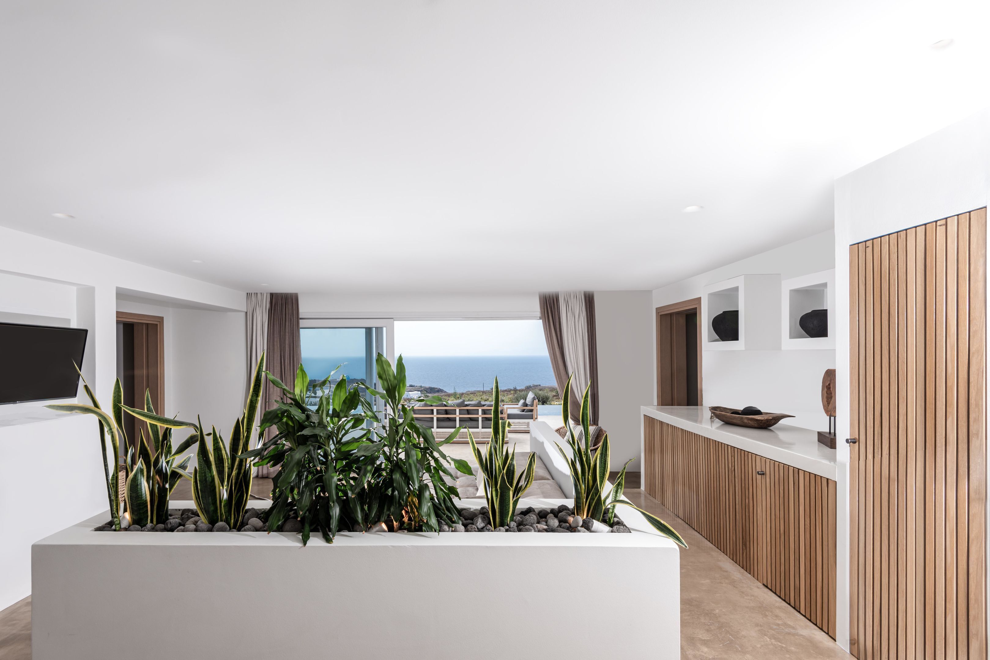 Un saló modern amb una finestra gran, una taula de consol blanca i un arranjament de plantes en testos.