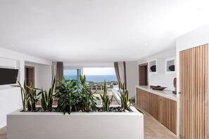 A modern living room with a large window, a white console table, and a potted plant arrangement. - Andronis Arcadia Hotel (Santorini)