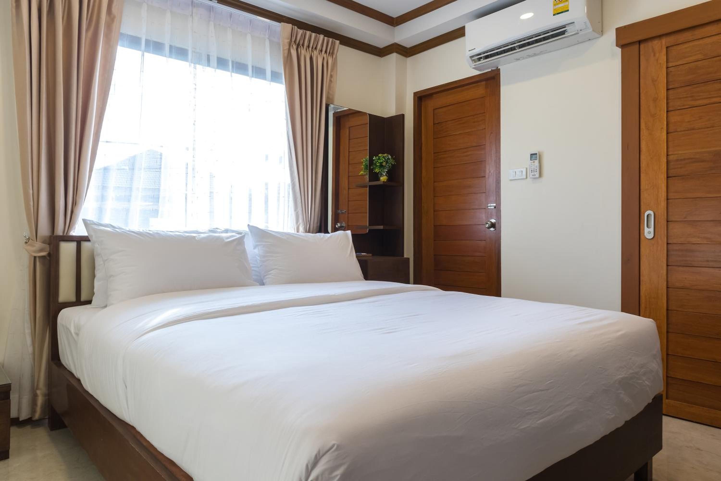 A hotel room with a large bed, wooden doors, an air conditioning unit, and a window with curtains.