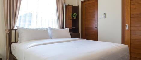 A hotel room with a large bed, wooden doors, an air conditioning unit, and a window with curtains.