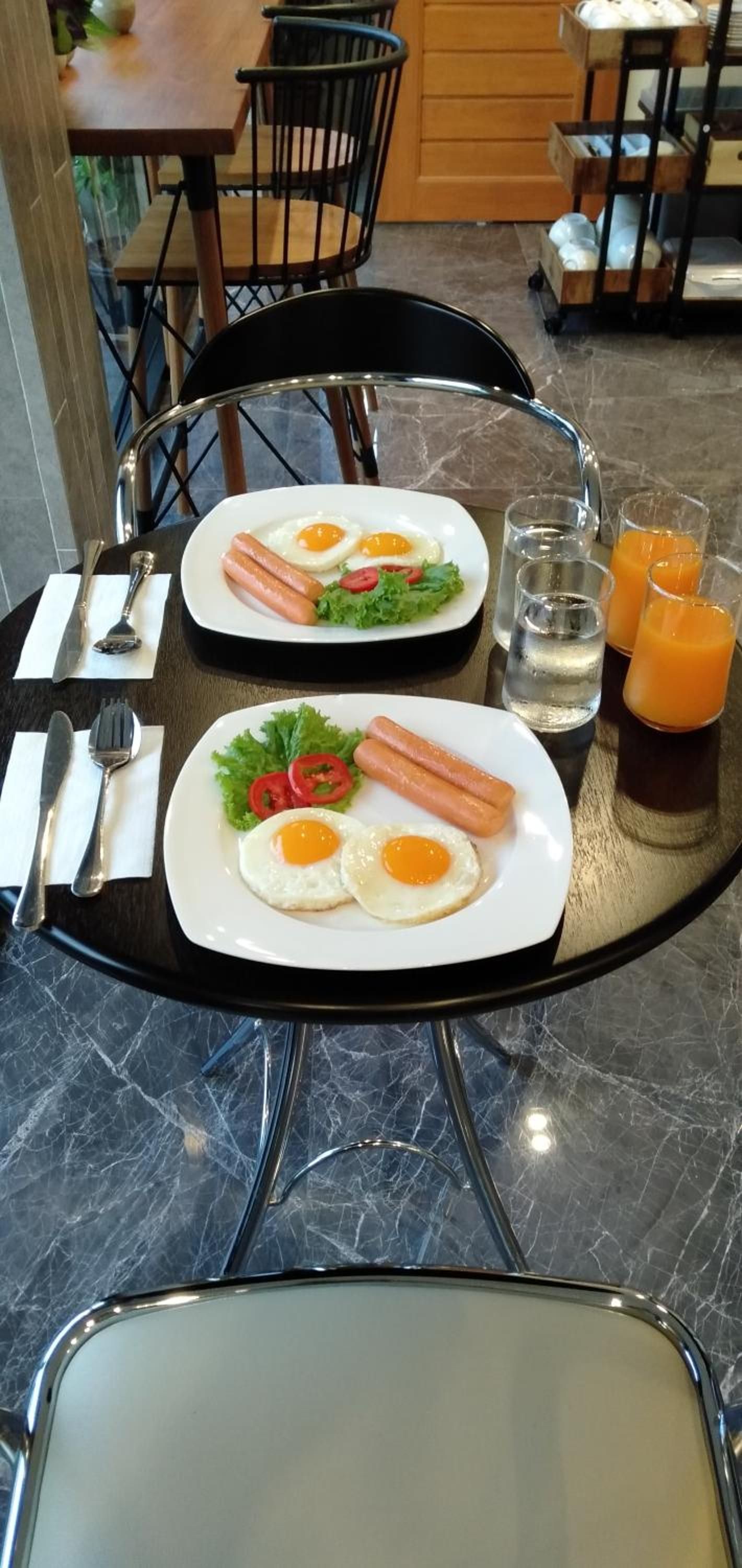 A dining table with plates of food, cutlery, and glasses of orange juice.