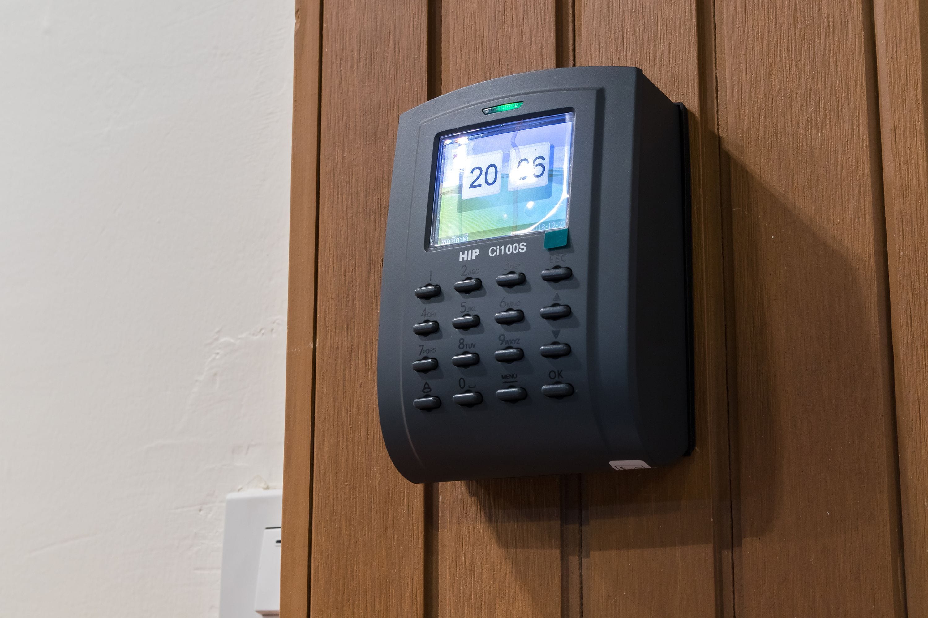A black electronic keypad with a digital display on a wooden wall.