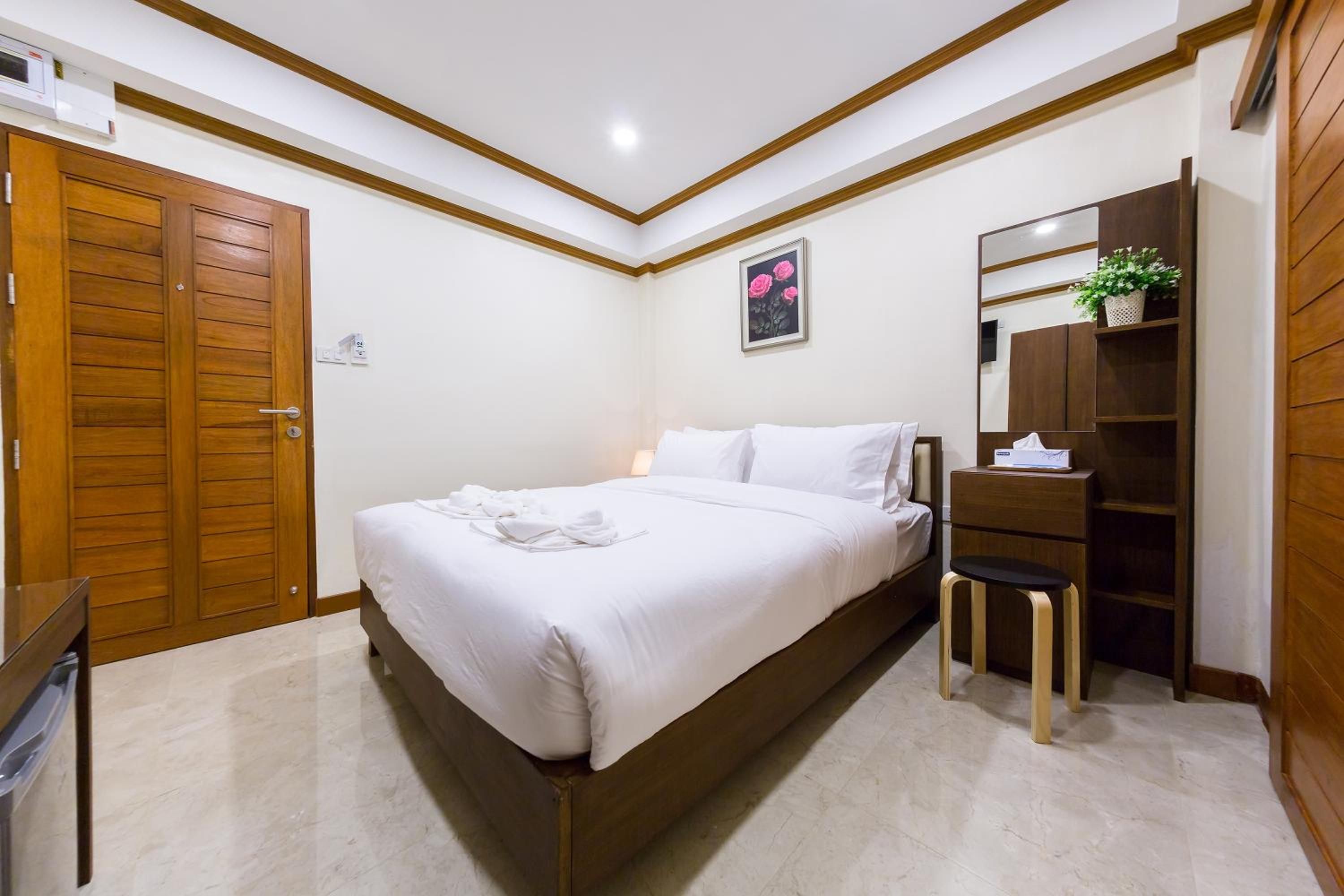 A bedroom with a bed, a wooden wardrobe, a small stool, and a mirror.