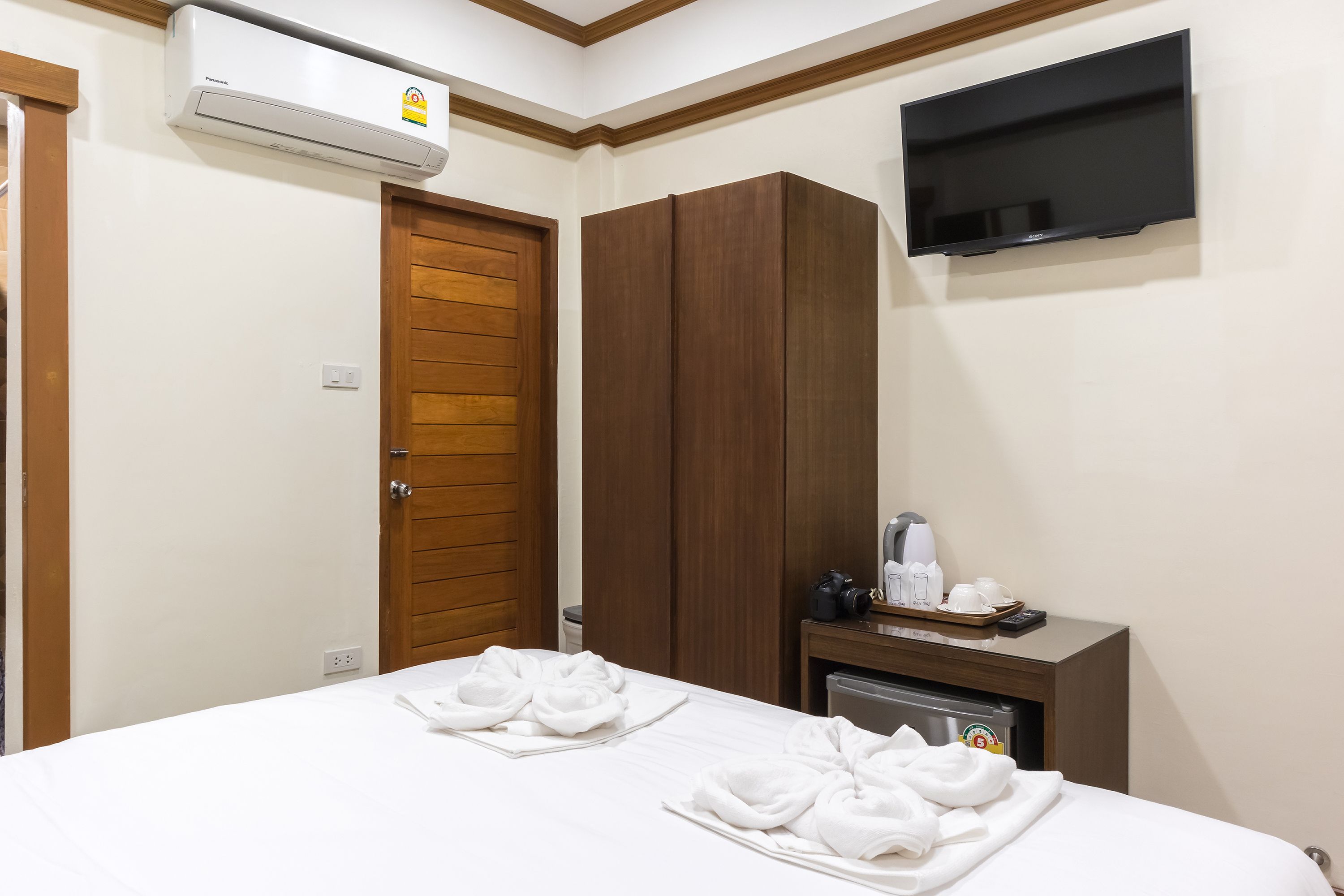 A hotel room with a bed, a wardrobe, a television, and a minibar.