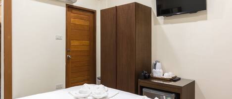A hotel room with a bed, a wardrobe, a television, and a minibar.