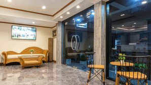 A lobby with a polished marble floor, a wicker sofa, a small table with chairs, and a large TV screen displaying a mall scene. - Suthep Home & Hostel (Bangkok)