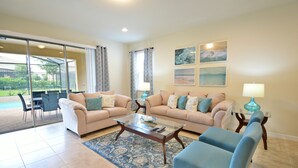 A living room with two sofas, a coffee table, and a TV. There is a glass door leading to a patio area with a pool.