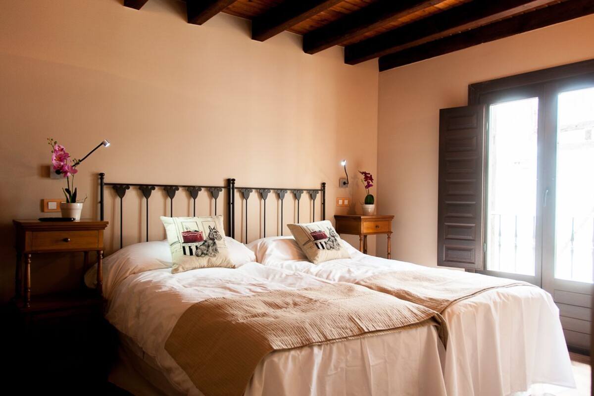A double bed with a wooden headboard, a bedside table with a lamp, and a window with shutters.