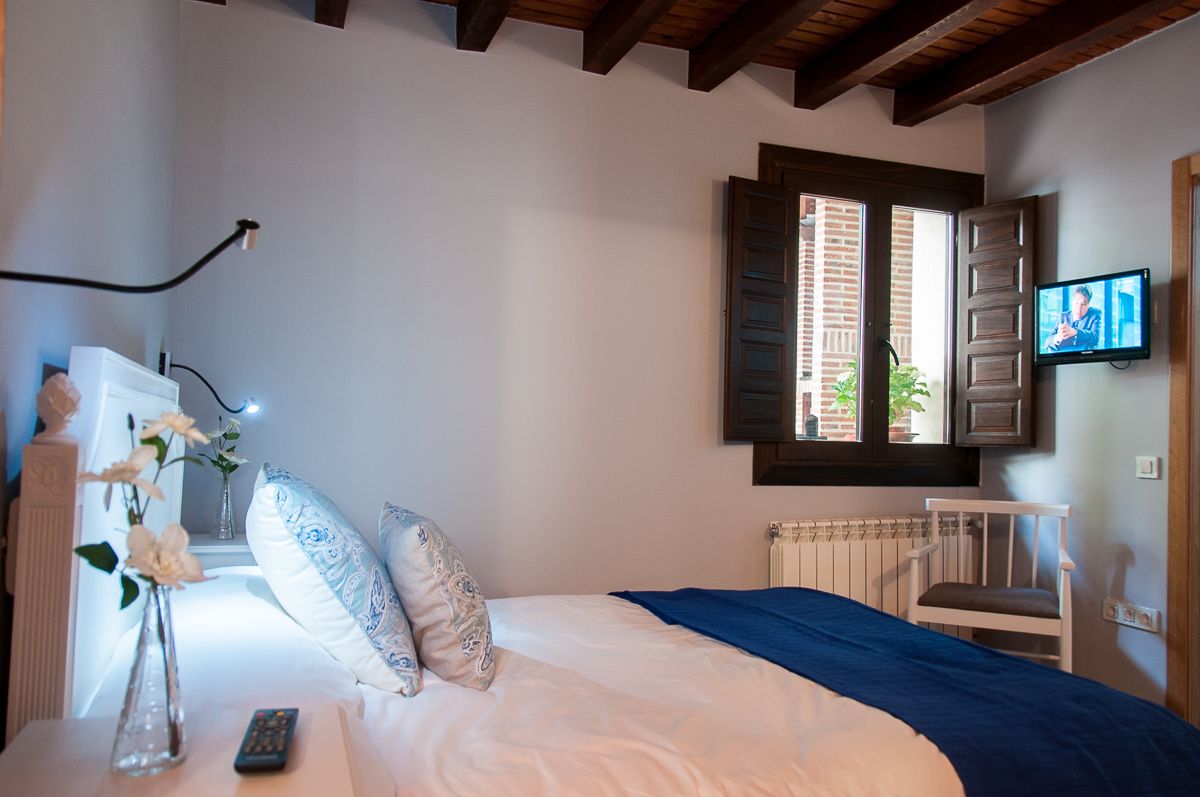 Un dormitorio con una cama, una silla, un televisor, un ventanal y un jarrón con flores.