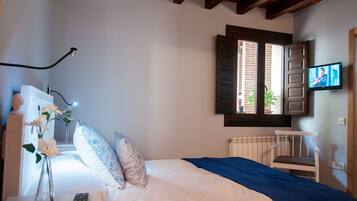 Un dormitorio con una cama, una silla, un televisor, un ventanal y un jarrón con flores.