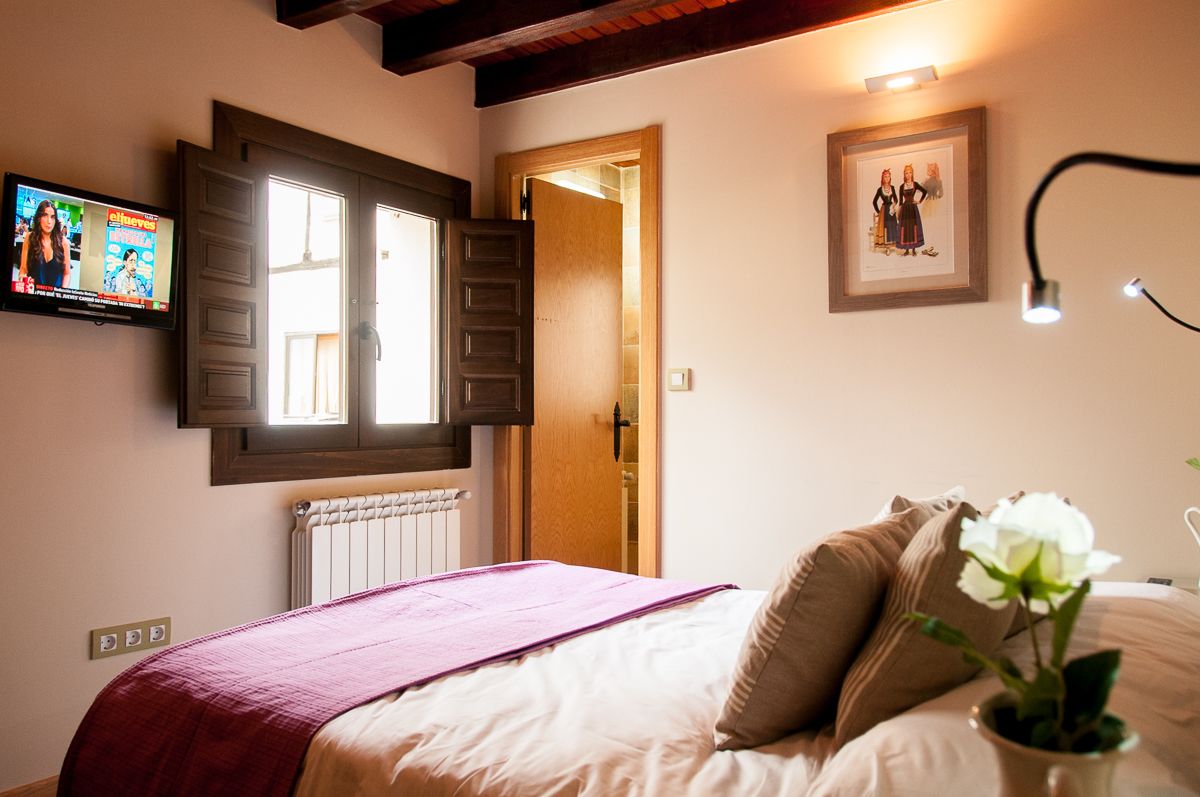 Un dormitorio con una cama, un televisor montado en la pared, un cuadro enmarcado y una puerta que da a otra habitación.