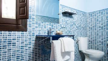Un bany amb rajoles de mosaic blaus, un vàter blanc, un lavabo amb mirall i un suport per a tovalloles.