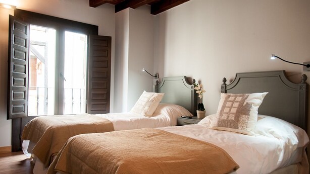 A room with two beds, a wooden ceiling, a window with shutters, and a nightstand with a lamp and flowers. - Hotel Rural Princesa Kristina (Covarrubias)