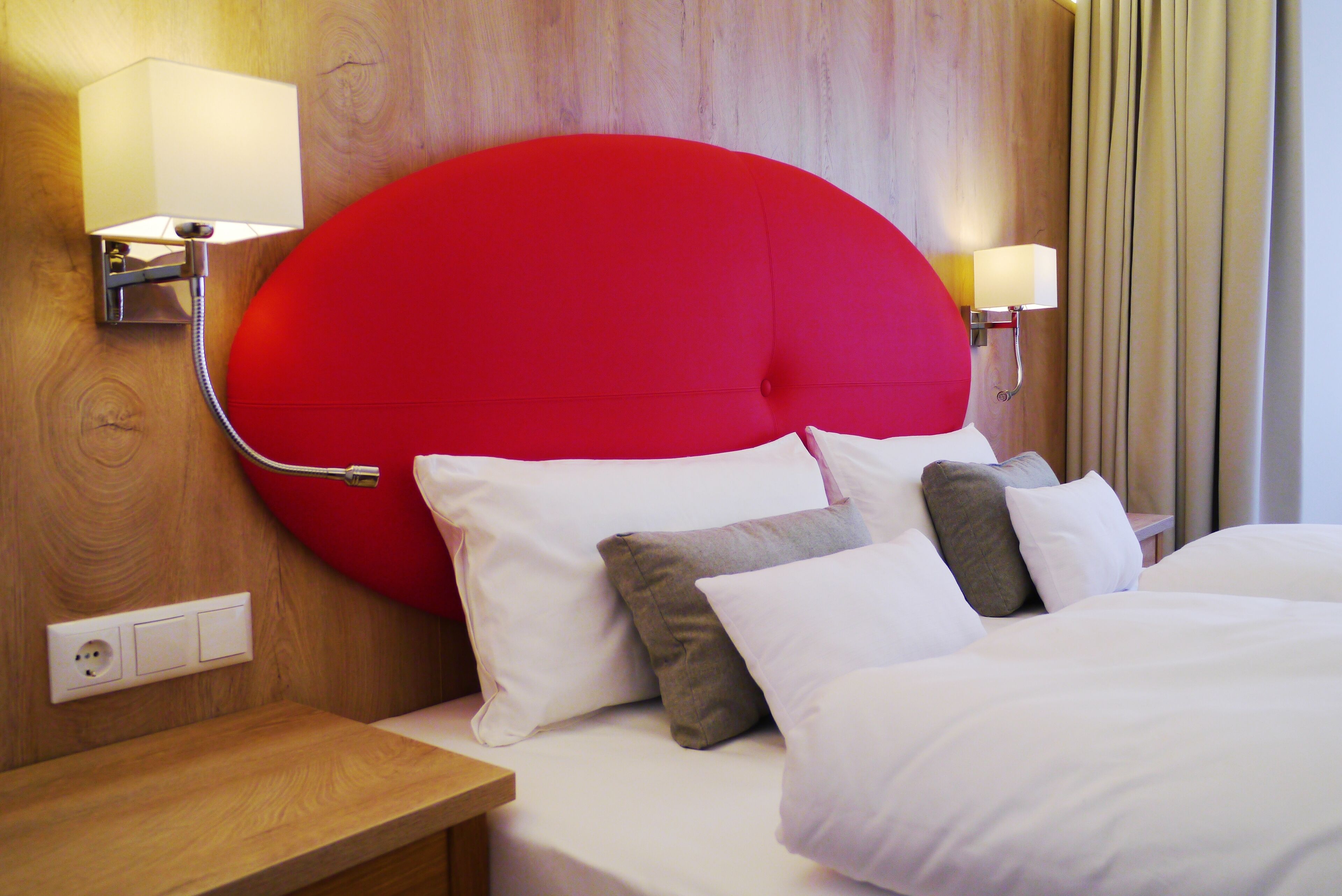 A hotel room with a large red headboard, white bedding, and two bedside lamps.