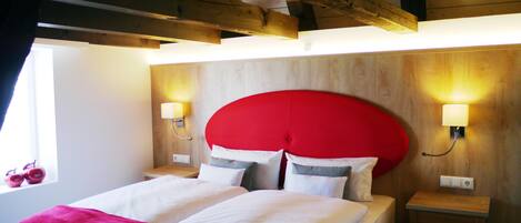 Un dormitorio con techo de madera, cabecero rojo, dos mesitas de noche con lámparas y una ventana con cortinas.