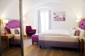 A bedroom with a large bed, a chair, a desk, and a mirror. - Das Brunners Hotel (Weiden in der Oberpfalz)