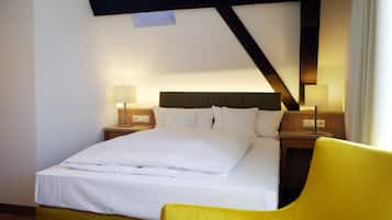Une chambre d’hôtel avec un lit bien fait, deux tables de chevet avec des lampes et un fauteuil jaune.