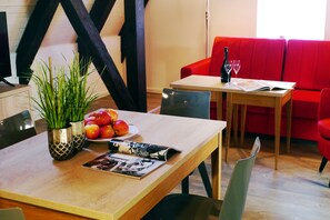 A dining area with a wooden table, a red couch, and a bottle of wine. - Das Brunners Hotel (Weiden in der Oberpfalz)