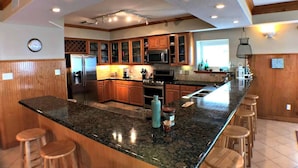 A kitchen with granite countertops, wooden cabinets, and a central island with stools. - Atlantis - Oceanfront Seating at its Finest! (Freeport)