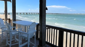 A wooden deck with white chairs and a table, overlooking a beach and a pier. - Atlantis - Oceanfront Seating at its Finest! (Freeport)