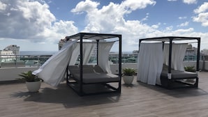 Una terraza en la azotea con dos camas con dosel, plantas en macetas y vistas a la ciudad y al mar.