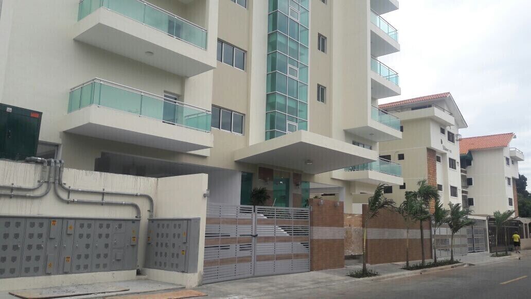 A multi-story building with balconies, a gated entrance, and a street view.