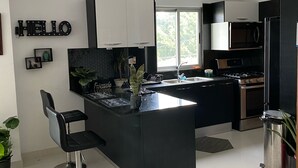 Una cocina moderna con una isla central, taburetes negros, electrodomésticos de acero inoxidable y un letrero con la palabra 'HELLO' en la pared.