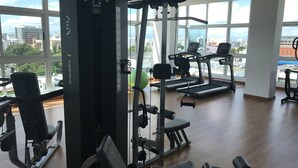 Un gimnasio con equipo cardiovascular, máquinas de pesas y vistas a la ciudad a través de amplias ventanas.